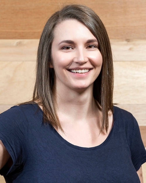 Headshot of a woman in a dark blue shirt against a wooden background.