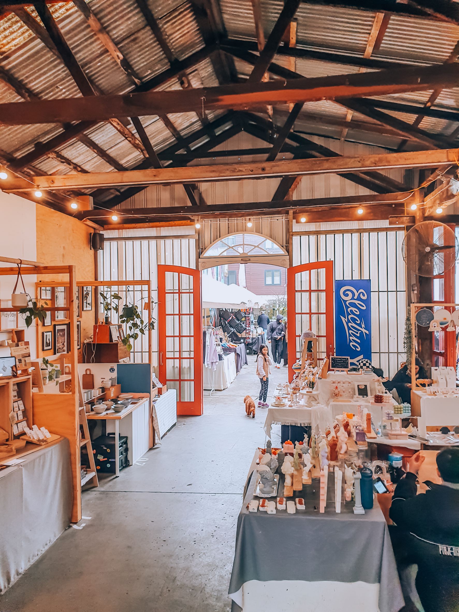 Rose St Artists Market indoor area with wood panelled high ceilings and french red doors with small stall vendors selling handmade goods 