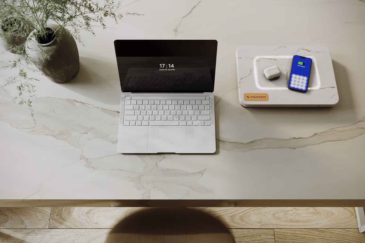 White marble desk with an open laptop, a white marble luxurious FreePower Valet wireless charging surface with AirPods and a smartphone, and a rustic vase with greenery.