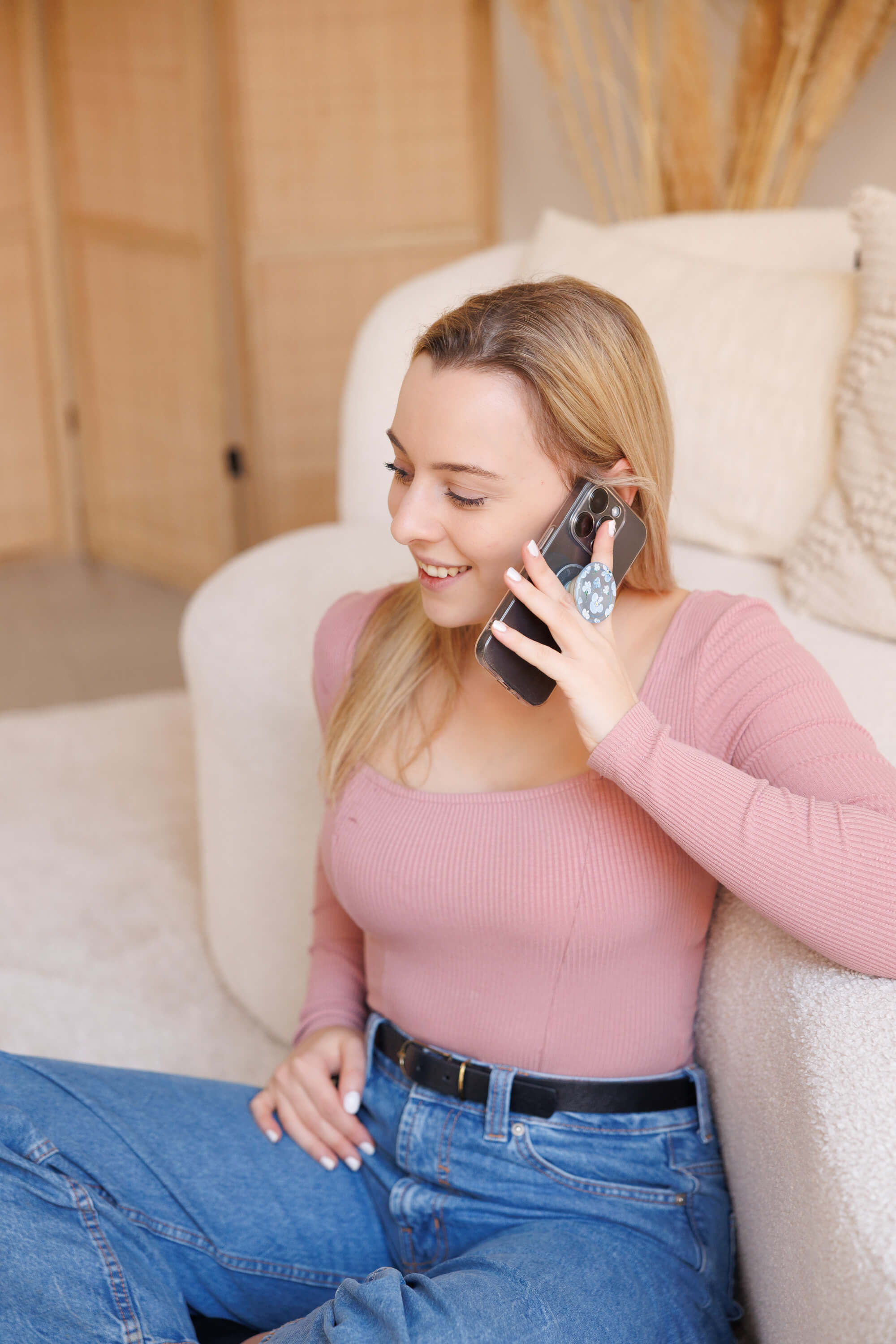 Tina Hörholdt telefoniert lächelnd, an ein helles Sofa gelehnt