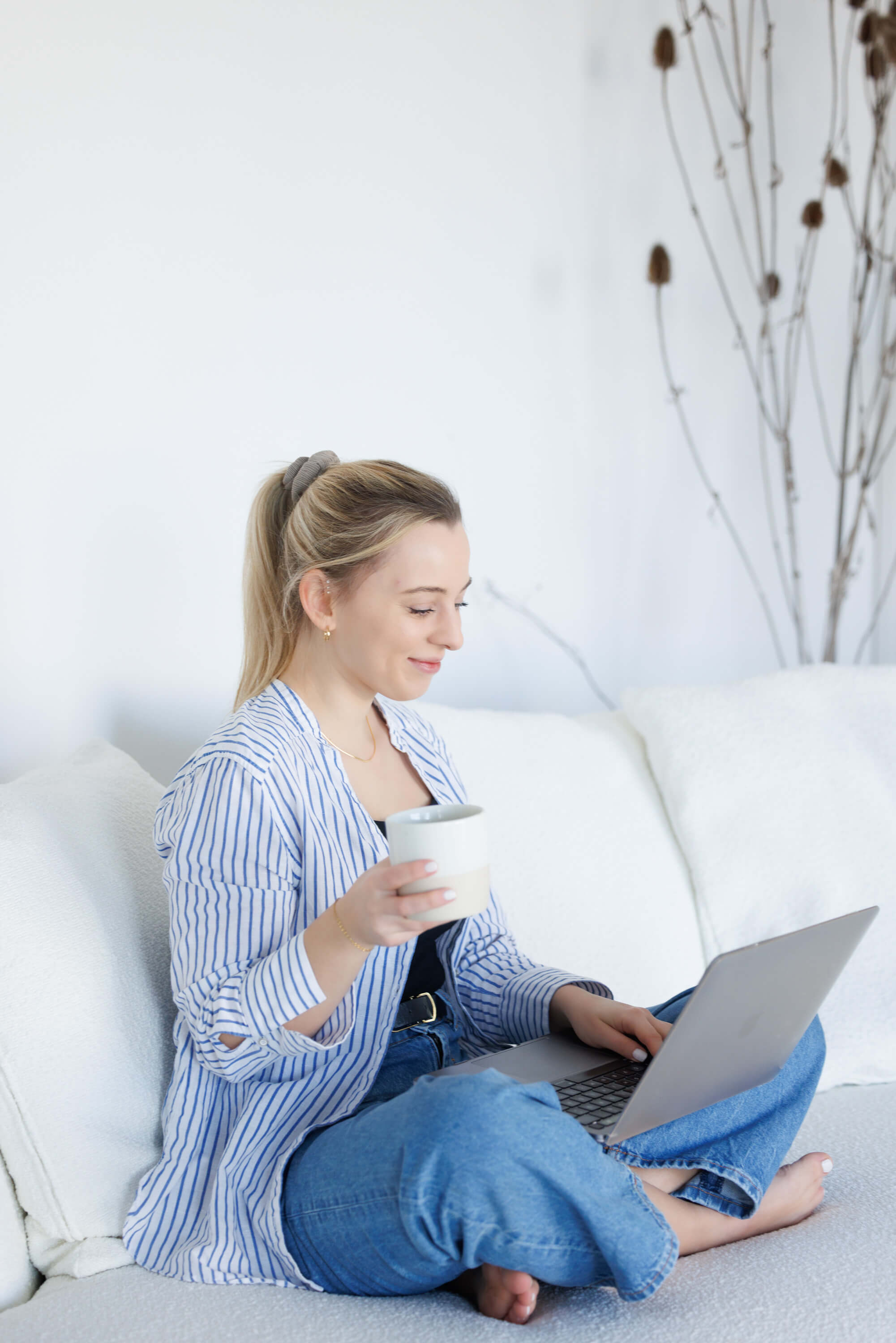 Tina Hörholdt mit Kaffeetasse und Laptop auf dem Boden vor einem weißen Sofa