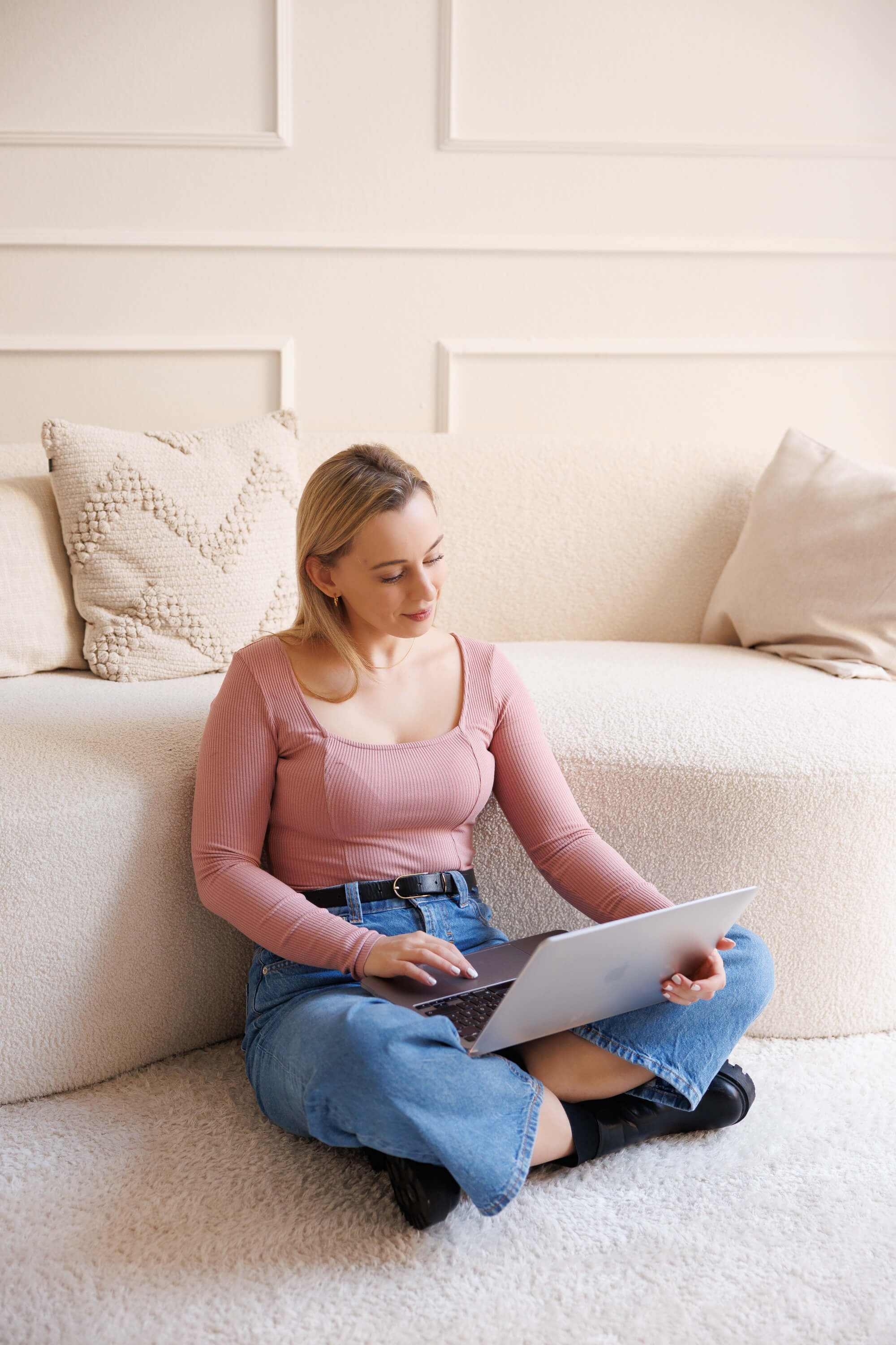 Tina Hörholdt sitting cross-legged in front of a light sofa, working on her laptop