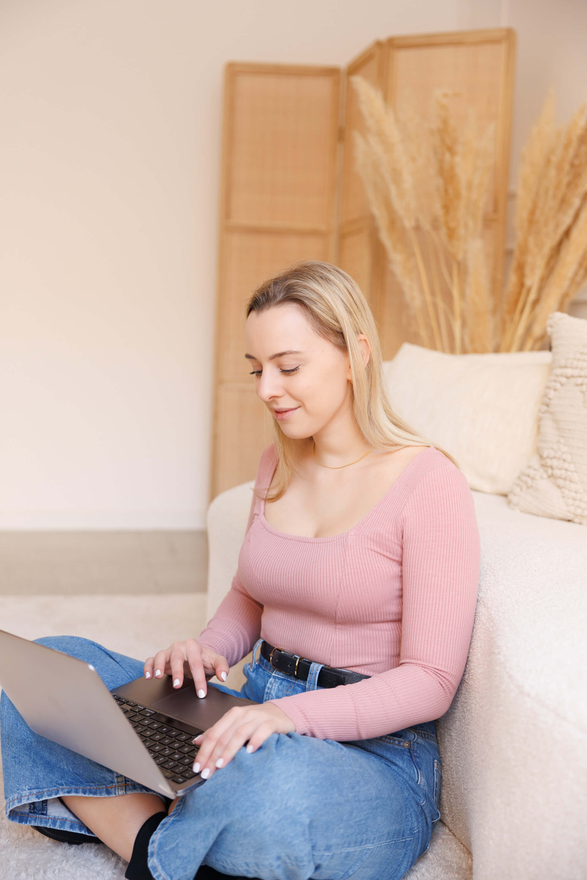 Tina Hörholdt in rosa Oberteil arbeitet am Laptop, an ein helles Sofa gelehnt
