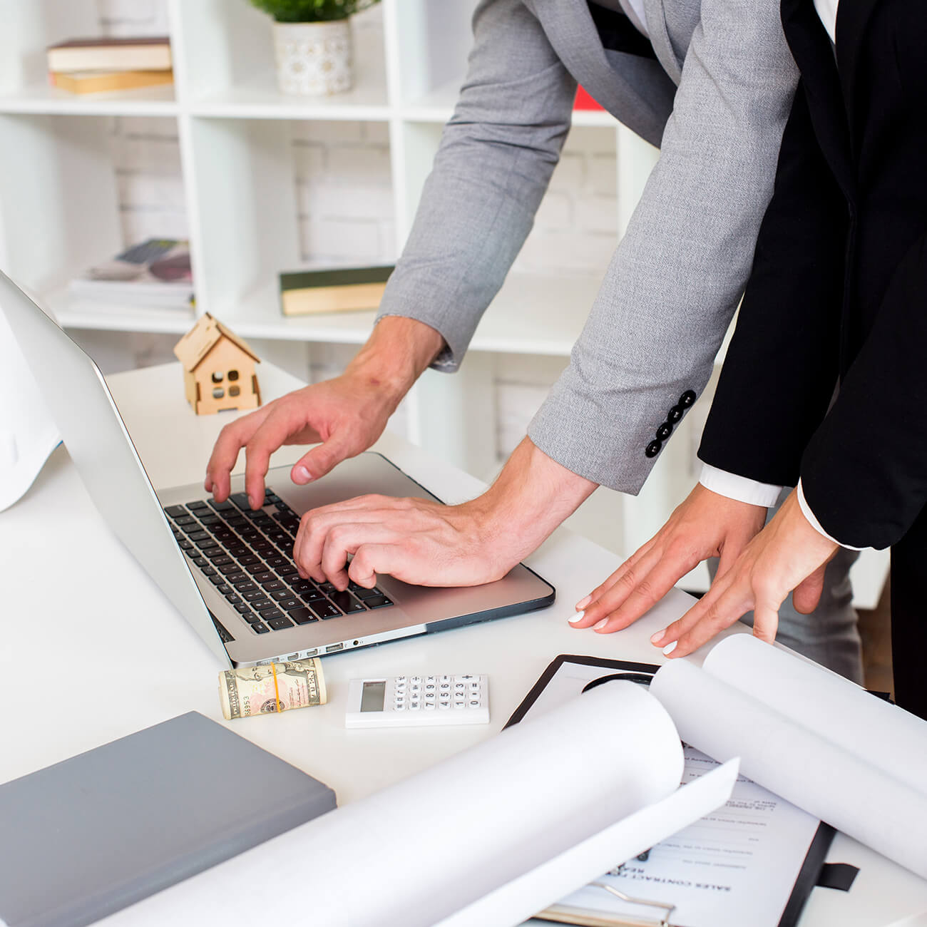Two people at a laptop next to a small model house and building plans