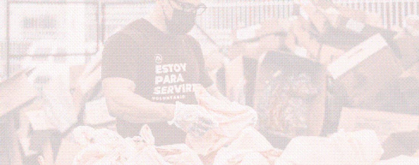 Volunteer wearing a mask sorts food items among stacked boxes in a warehouse or storage area.