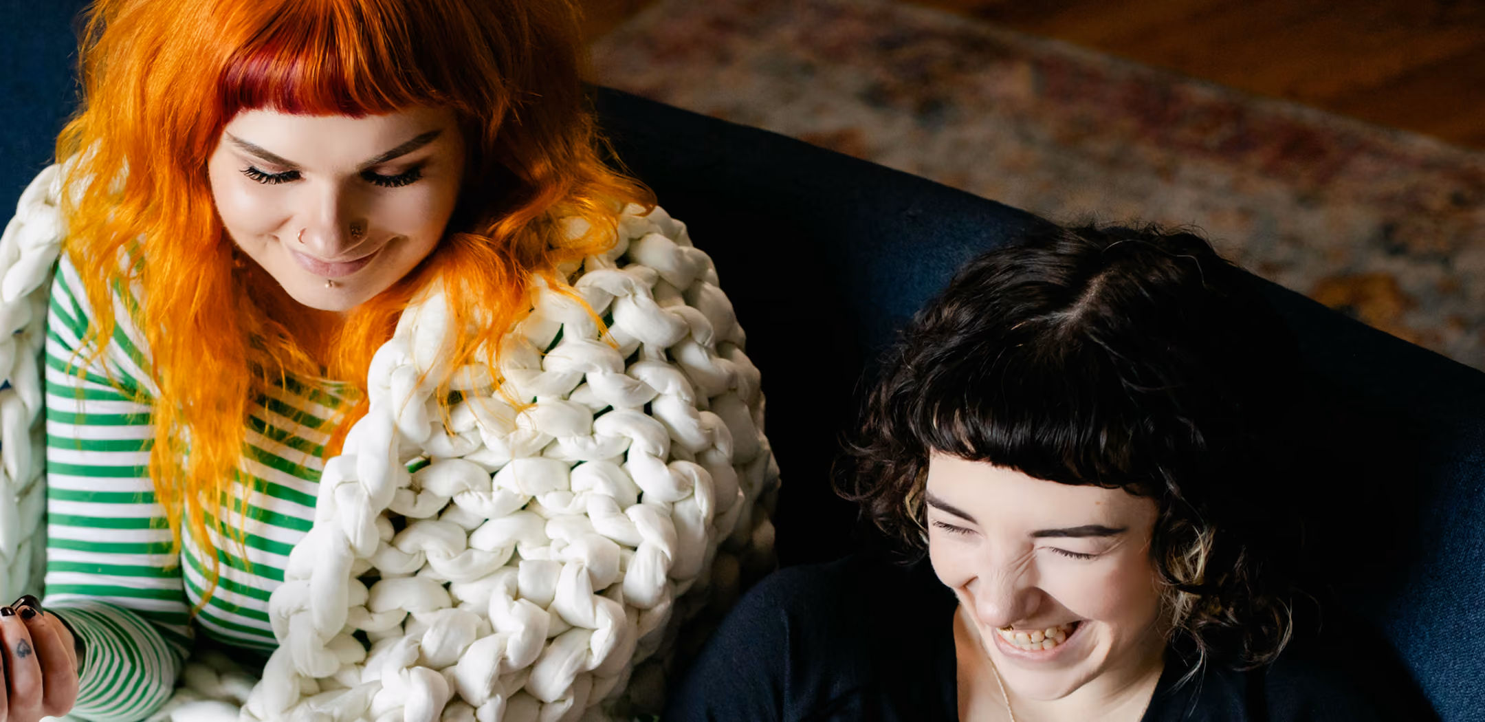 Two women laughing over a chunky knit blanket