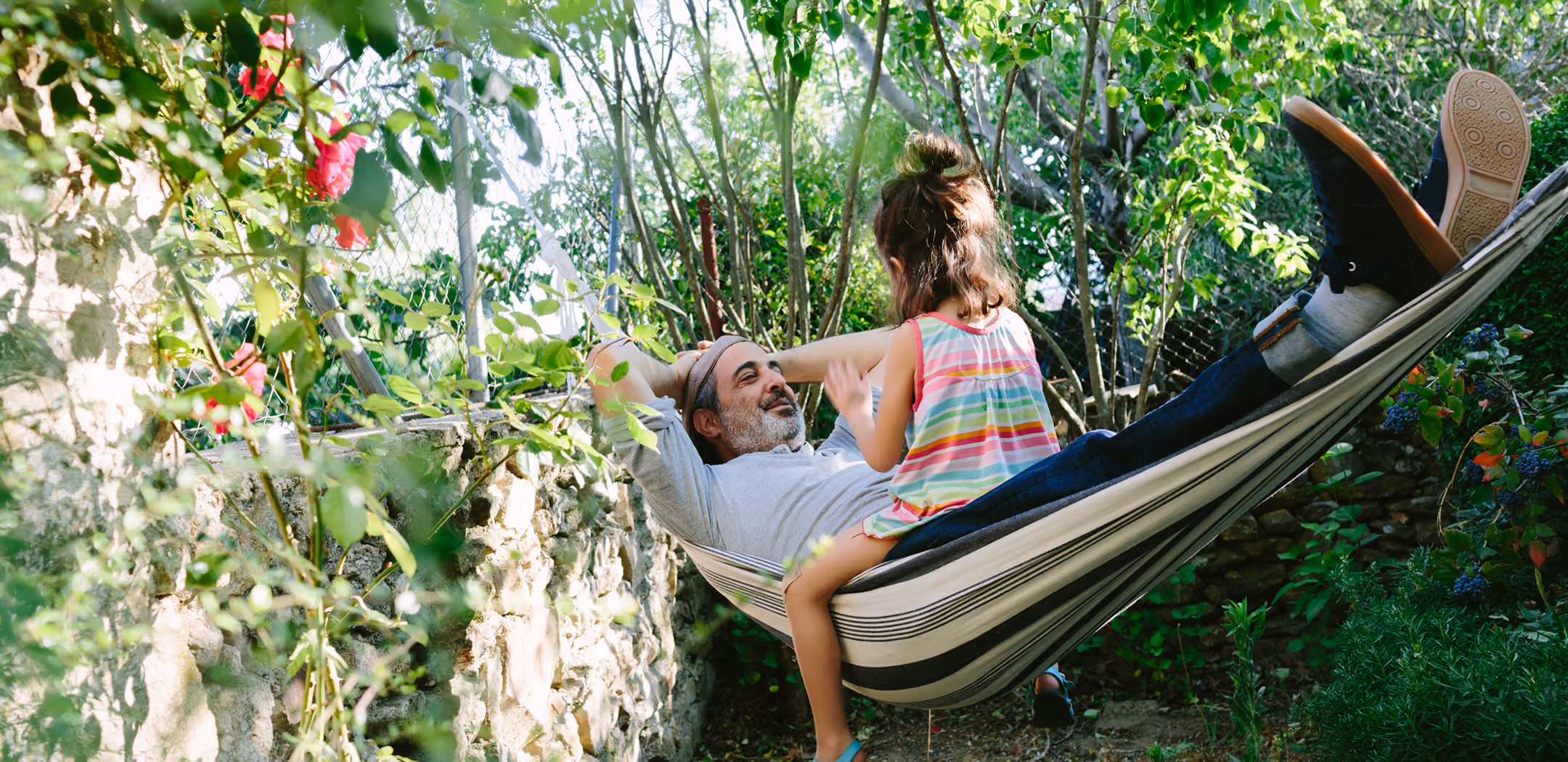 Man lying in a garden hammock talking with a young girl