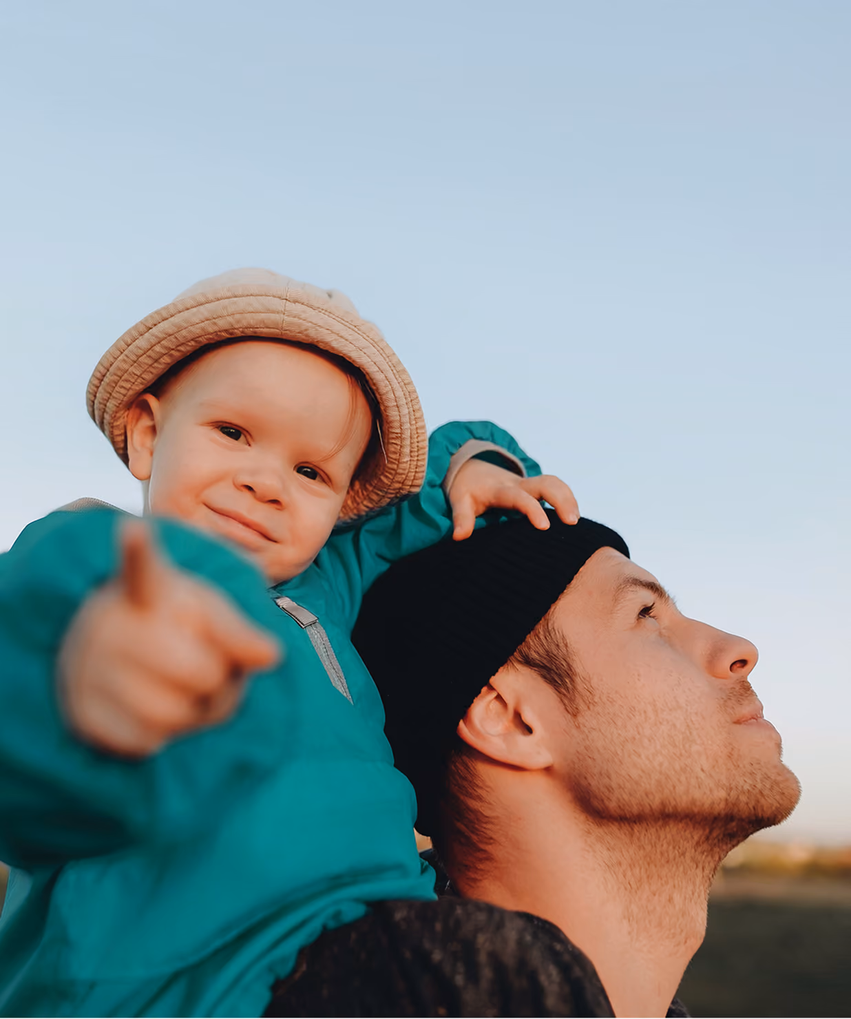 Man carrying a toddler on his shoulders as they both point ahead