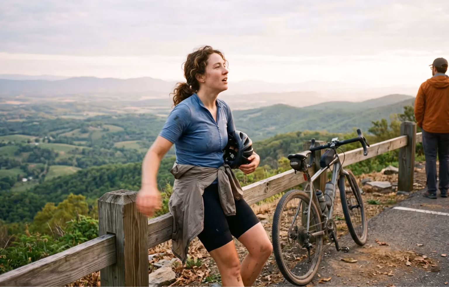 Woman standing beside her bicycle at a lookout over a valley