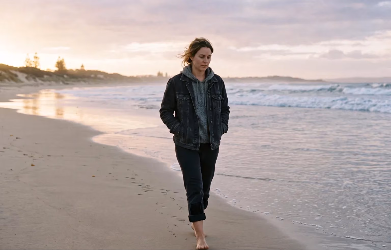 Woman walking barefoot along a beach at dawn