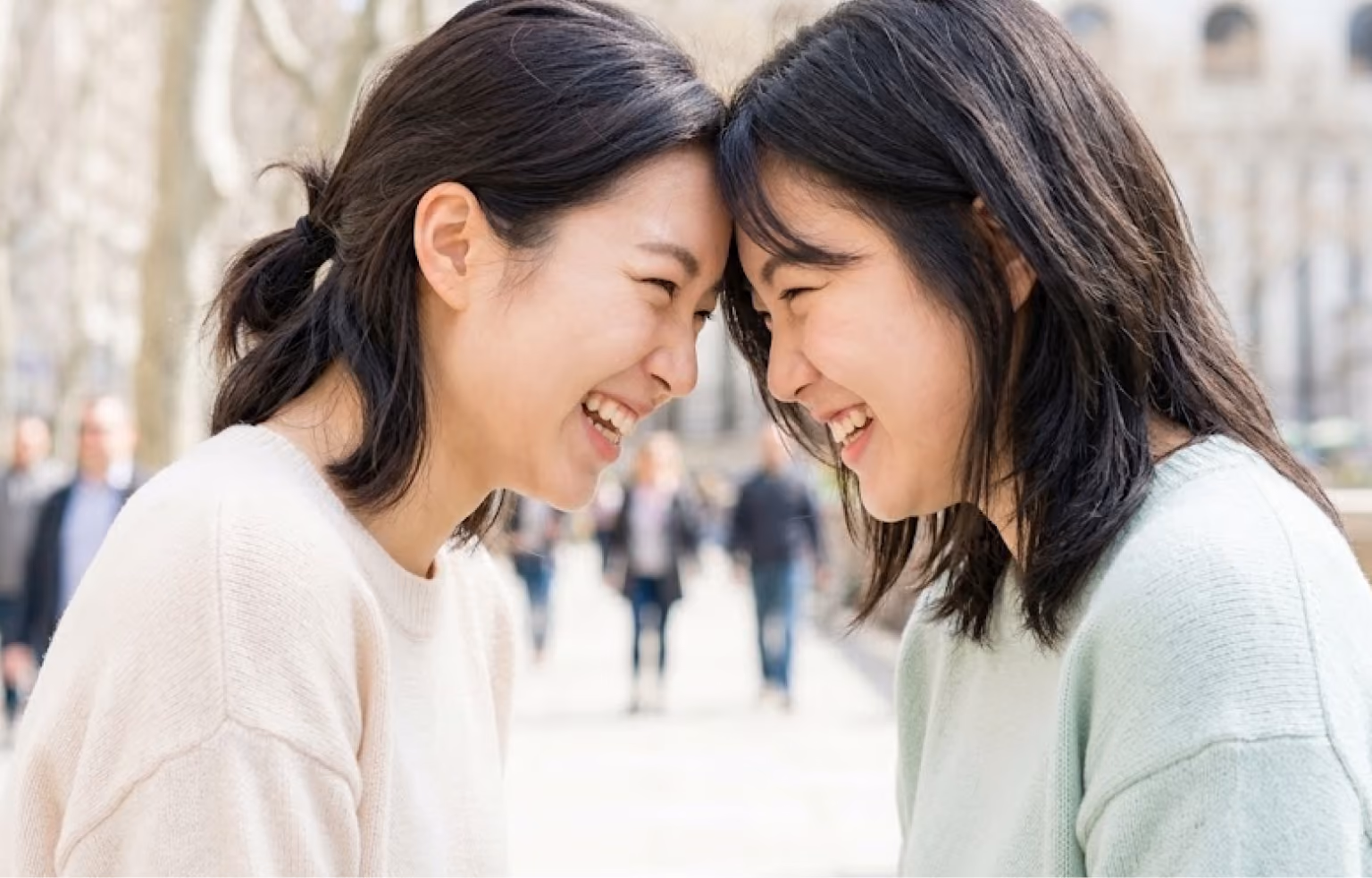 Two women touching foreheads and laughing on a busy street