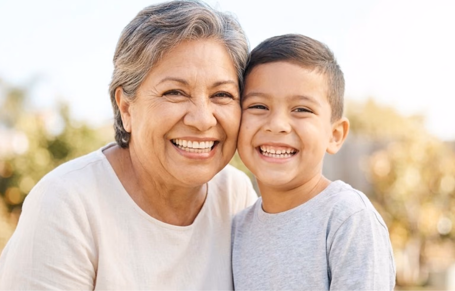 Grandmother and young grandson smiling cheek to cheek outdoors