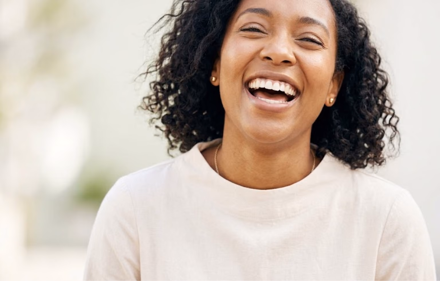 Young woman laughing outdoors in a cream sweater