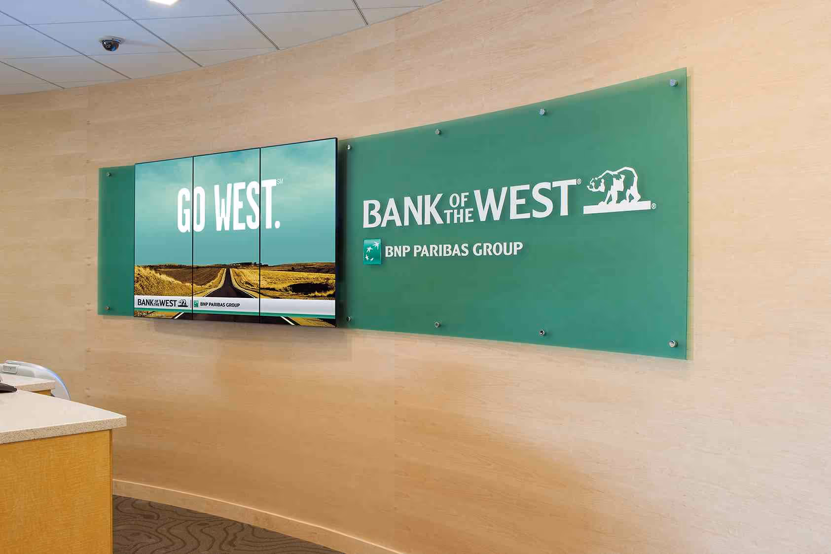 Bank branch behind teller digital sign and surround with signage.