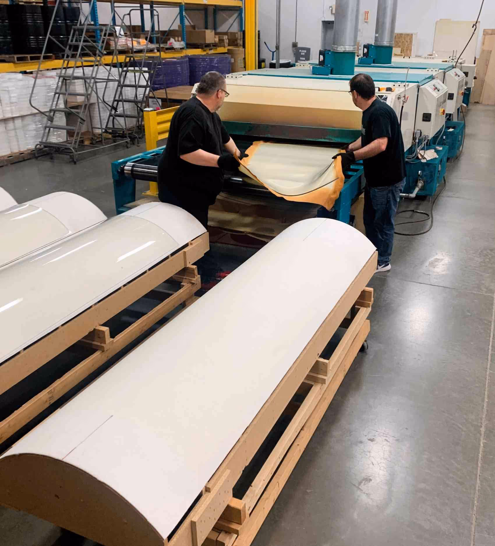 Two workers removing acrylic from a drape forming oven