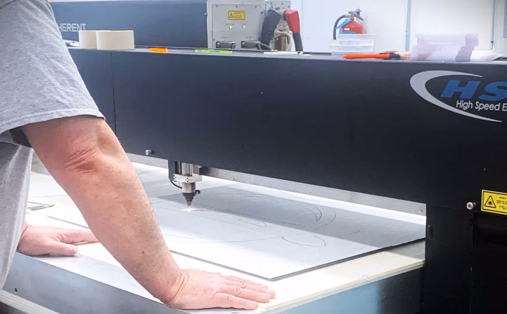 A worker monitoring a laser cutting a custom acrylic retail display part