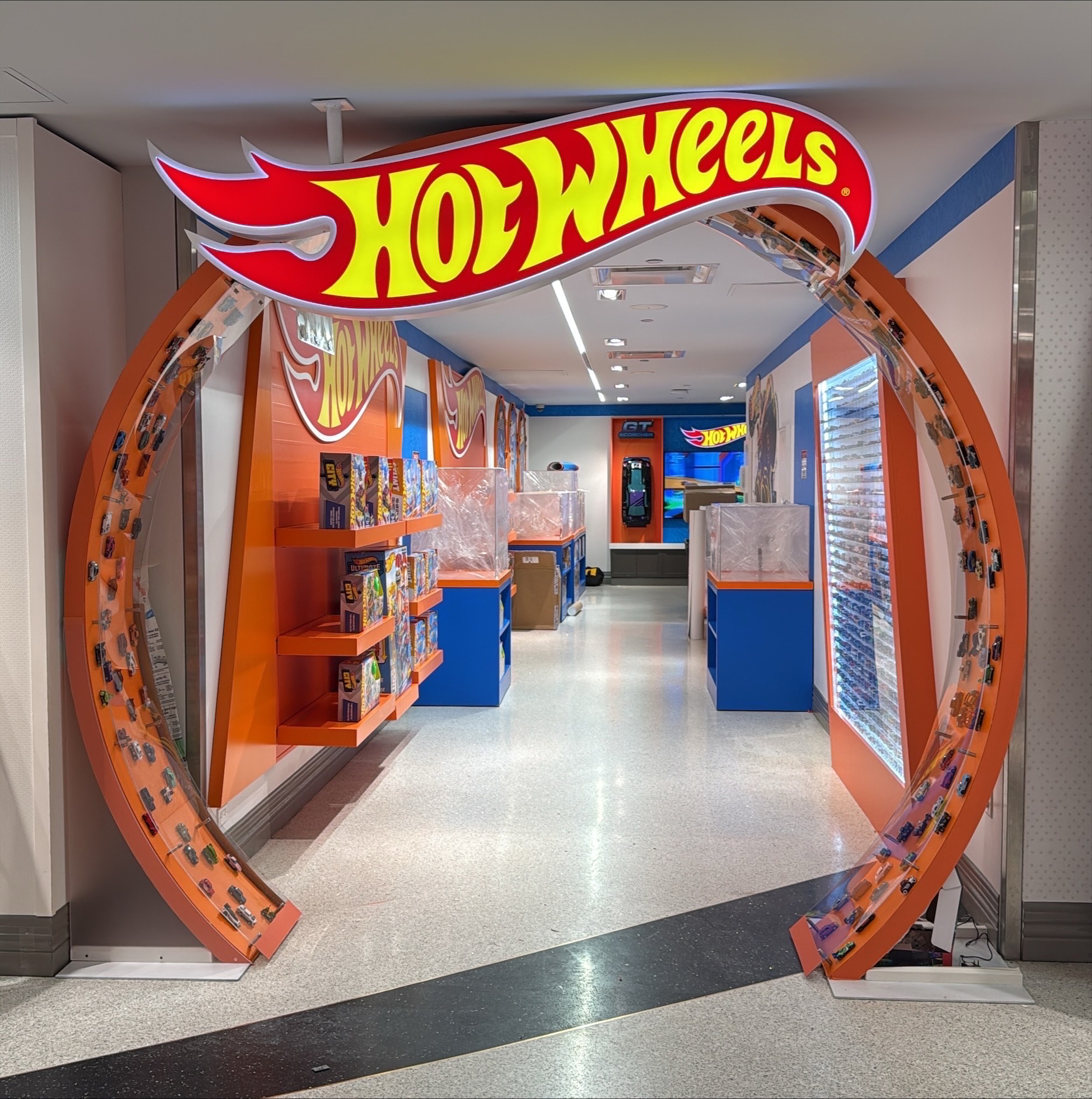 Entrance archway decorated with Hot Wheels logo and miniature toy cars on tracks on both sides.