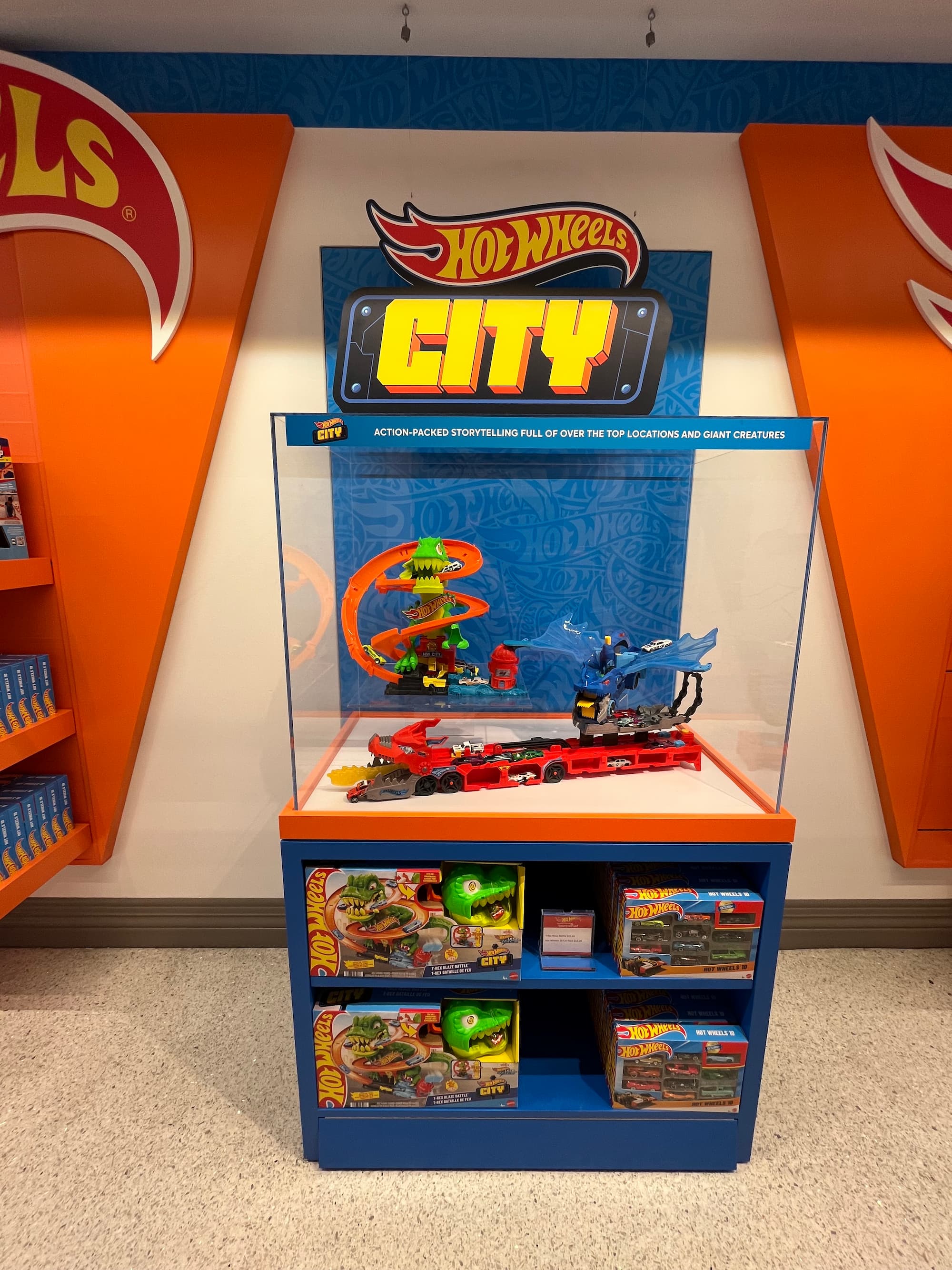 Hot Wheels City toy car playset with monster-themed tracks in a display case over boxed sets on shelves.