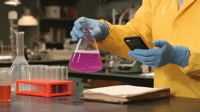 A lab scientist stirs a pink liquid in a conical flask.