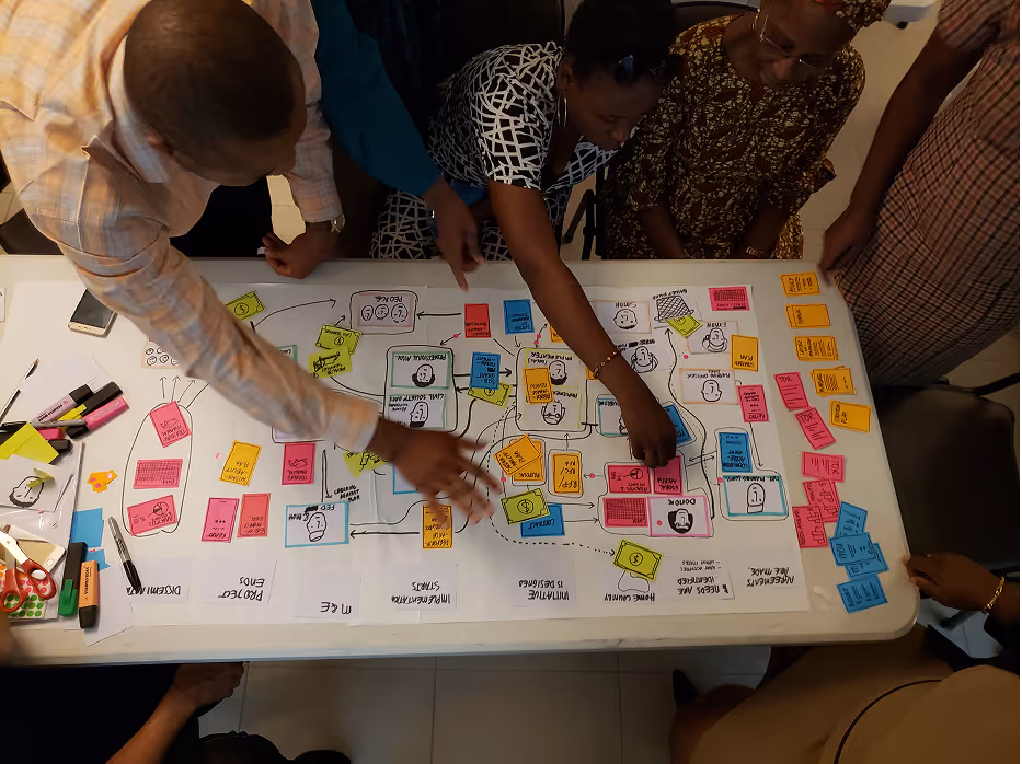 Aerial view of a small group of people at a workshop pointing to pieces of colourful paper laid out on a table
