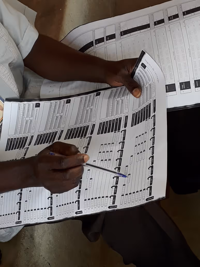Hands of a healthcare worker in Africa hold a pen and review a paper medical record on their lap