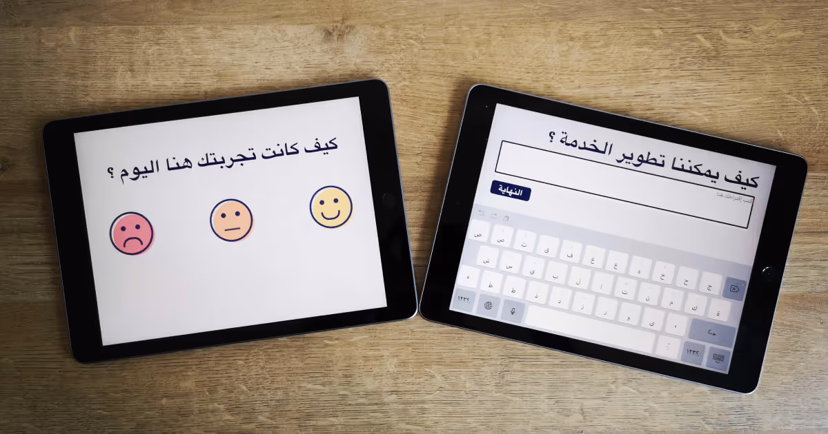 Two tablets on a wooden surface displaying Arabic survey questions about user experience, with one showing emoji options and the other a text input with an Arabic keyboard.