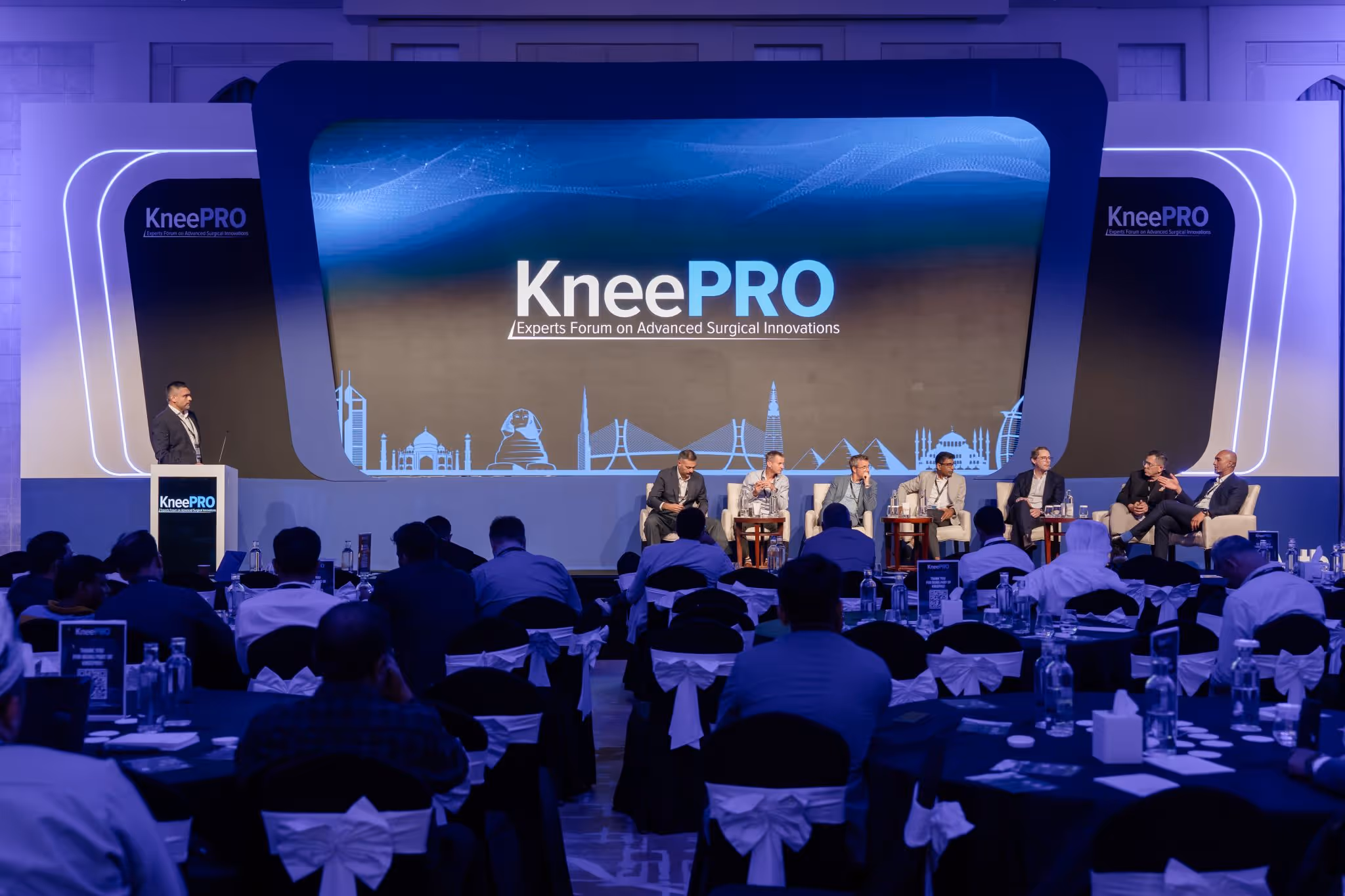 A group of people sitting at tables in front of a screen.