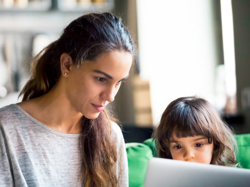 Parent works on a laptop while child watches.
