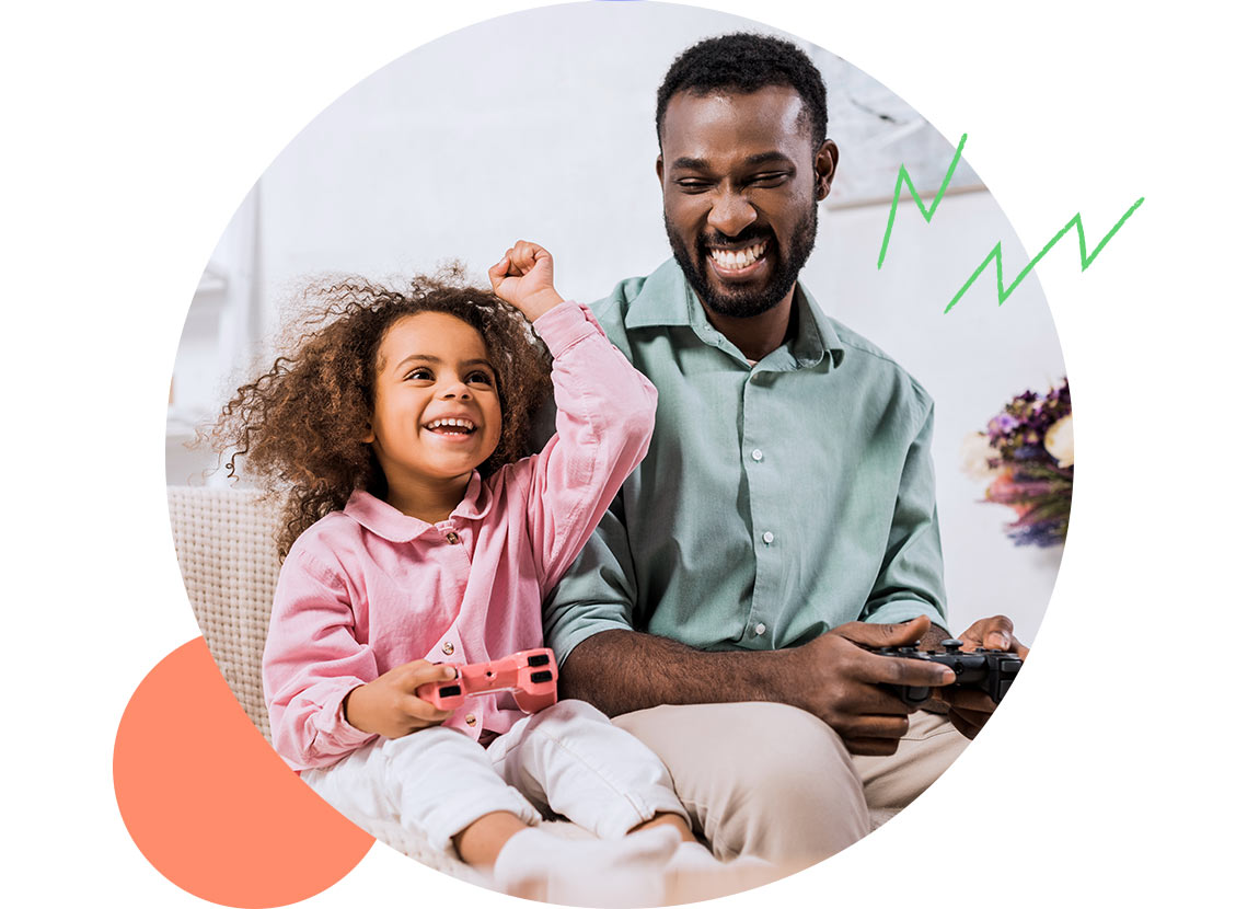 A young girl celebrating while playing video games beside her father