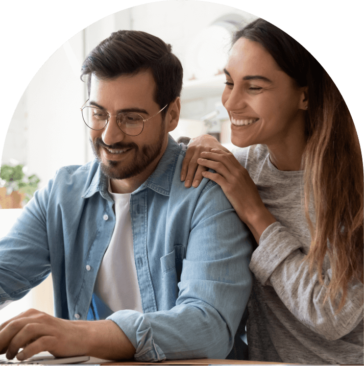 A young woman leans on a man's shoulder, looking at the laptop in front of them