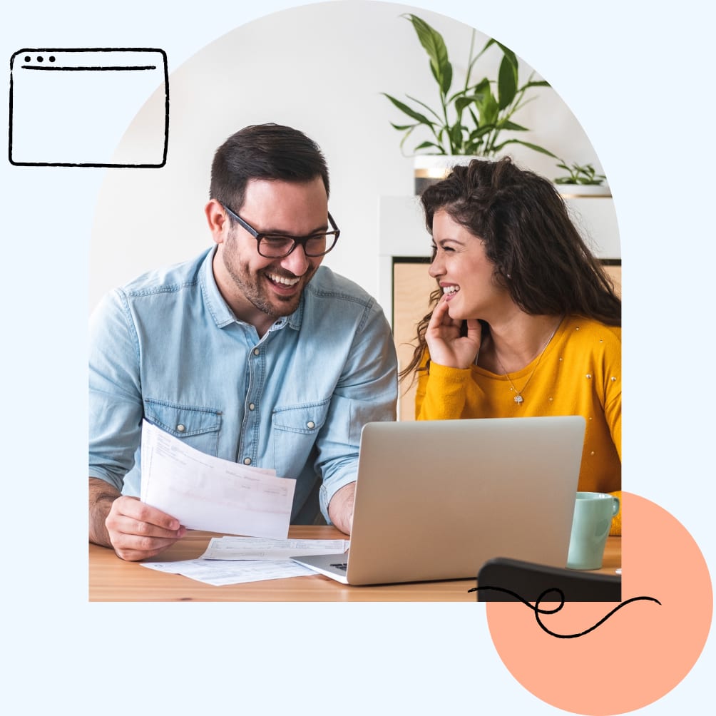 Smiling couple sitting at a table looking at laptop