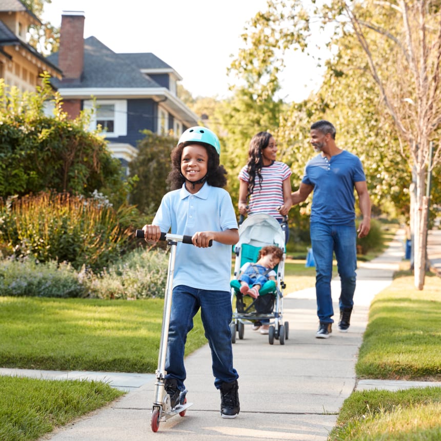 Family of four walking down suburban neighbourhood street on a sunny day