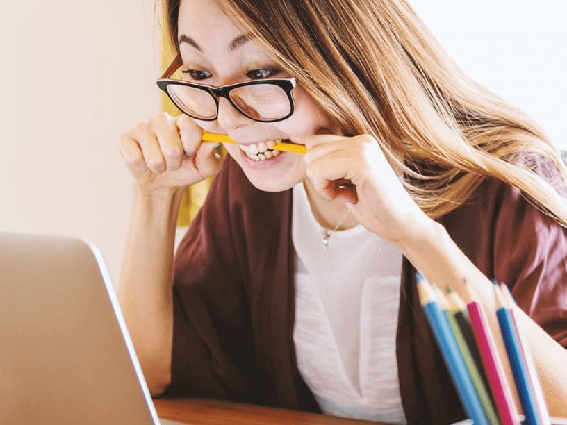Woman biting pencil in frustration while looking at laptop
