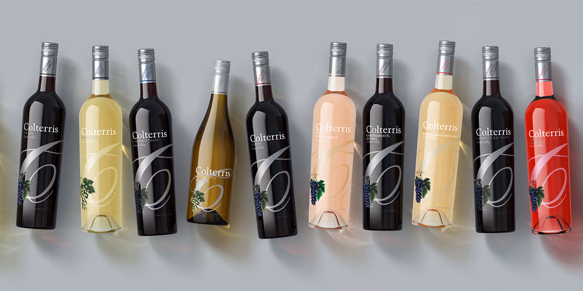 Ten Colterris wine bottles of various types and colors arranged side by side on a gray surface.