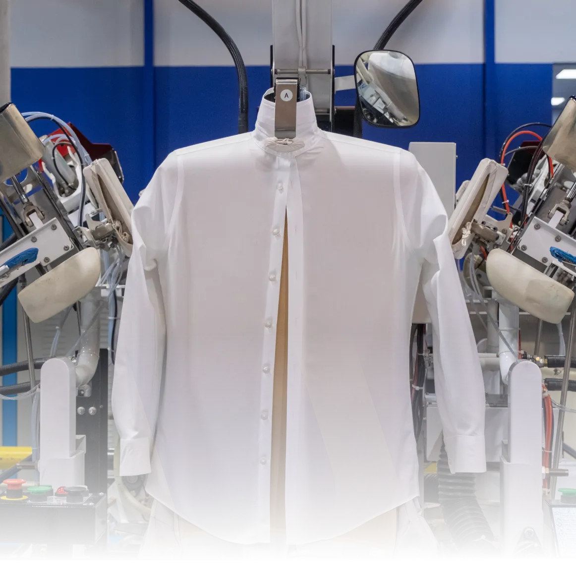 A white dress shirt displayed on a mannequin in a modern laundry facility, with automated pressing machines on either side.