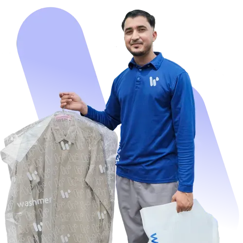 A man wearing a blue polo shirt holds a suit covered in plastic garment bag. He stands in front of a purple background, displaying a friendly demeanor while holding a white bag labeled "washer".