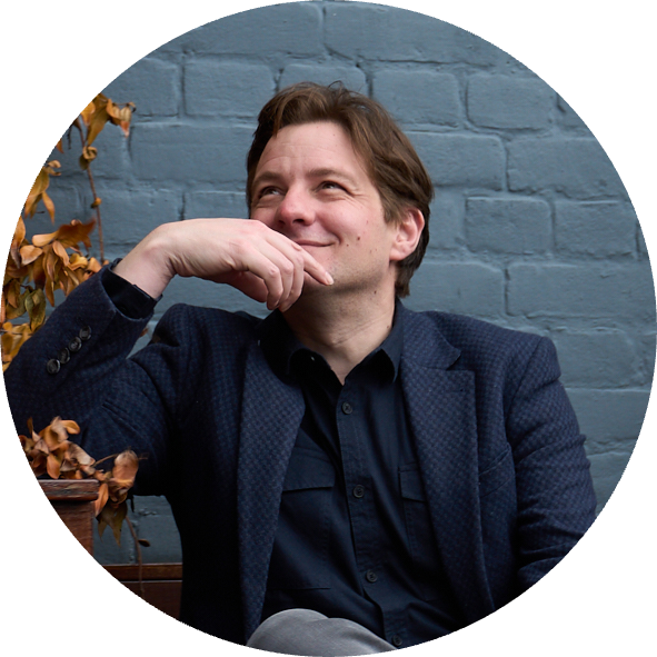 David, CEO of HR DataHub smiling thoughtfully on bench by blue brick wall and autumn leaves, illustrating insights on manufacturing salary guide and pay trends.