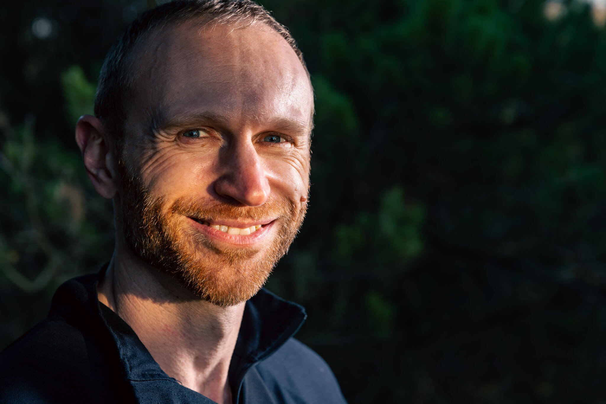 A man with a mole on his face smiles at the camera