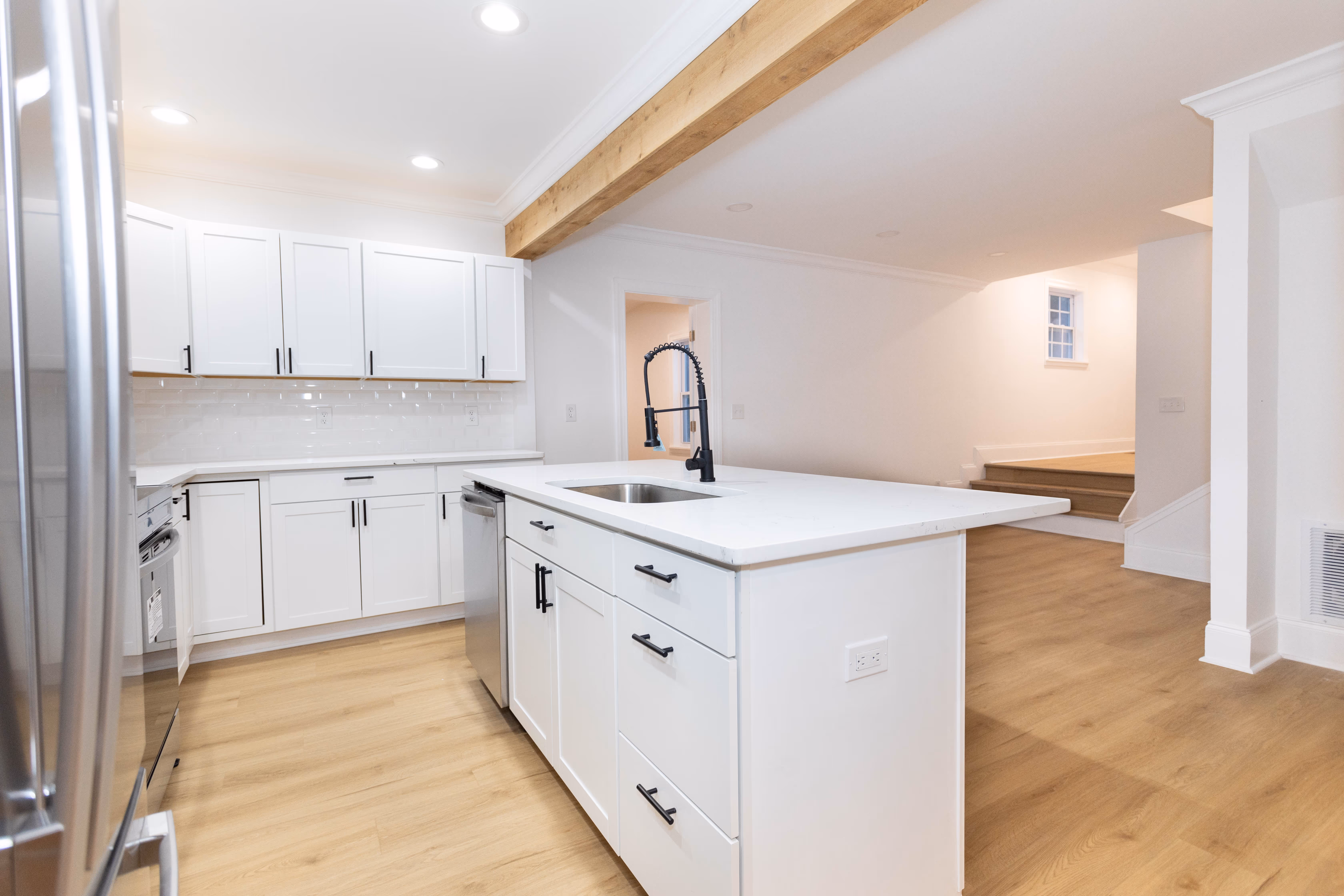 Modern kitchen with white cabinets, center island with sink, black faucet, and light wood flooring.