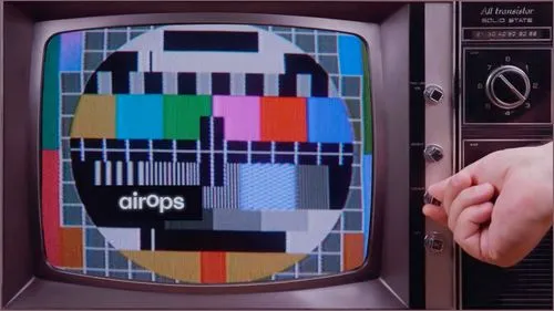 Hand adjusting color knob on old TV showing a multicolor test pattern with airOps text.