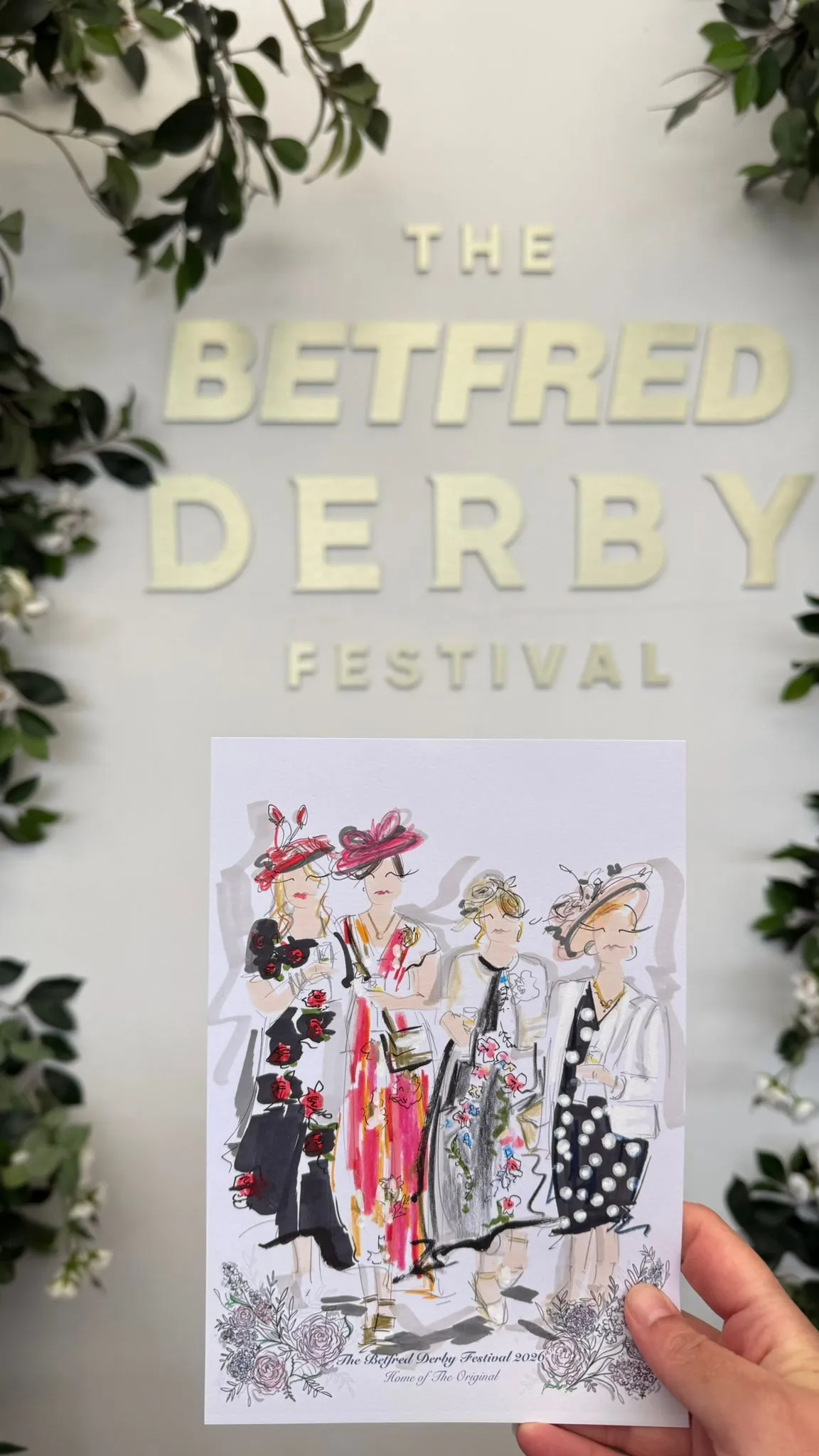 Hand holding illustrated card of four women in colorful dresses and hats at Betfred Derby Festival.