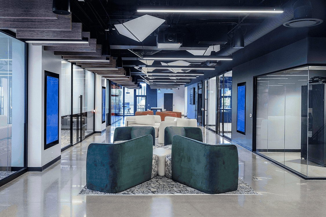 Modern conference room with a long white table surrounded by gray swivel chairs, large ceiling lights, and dual screens displaying 'nextspace'.