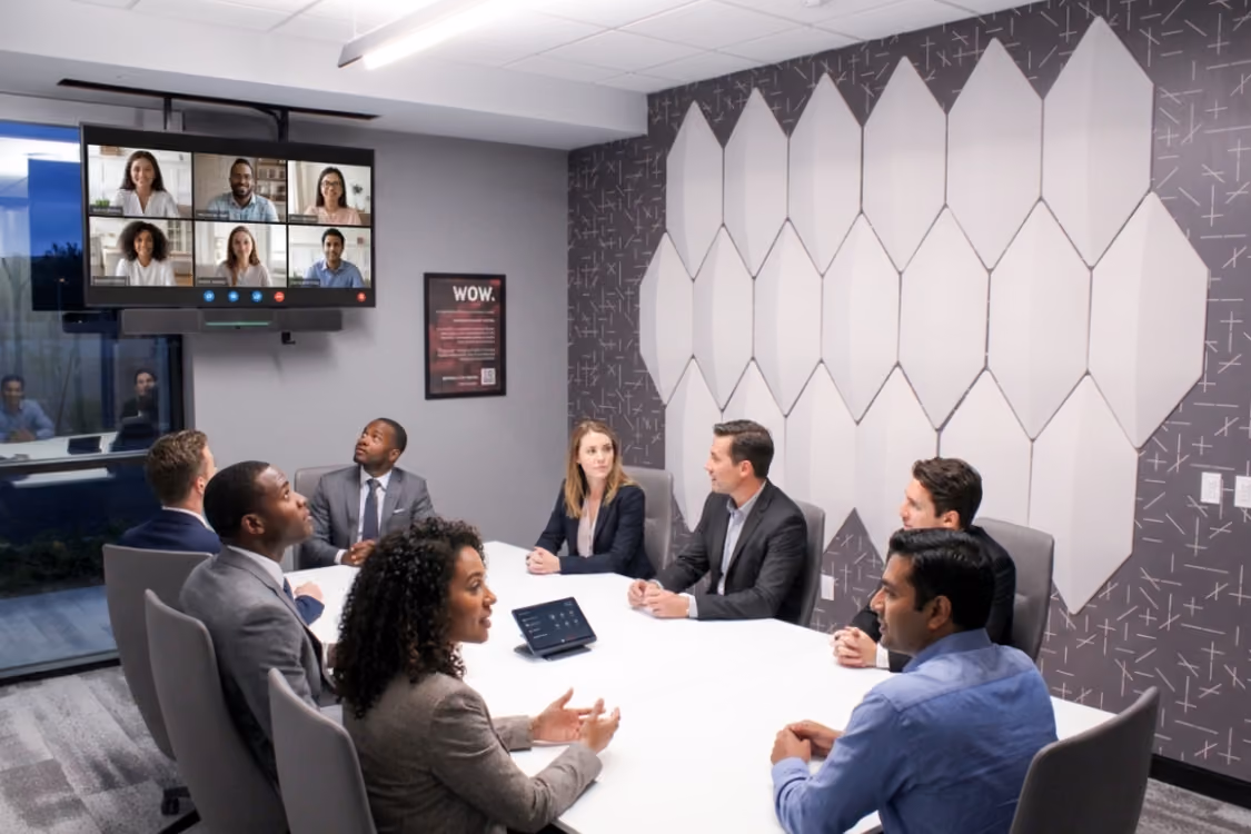Modern conference room with gray chairs around a white table, a wall-mounted screen displaying 'nextspace,' and a geometric patterned wall.