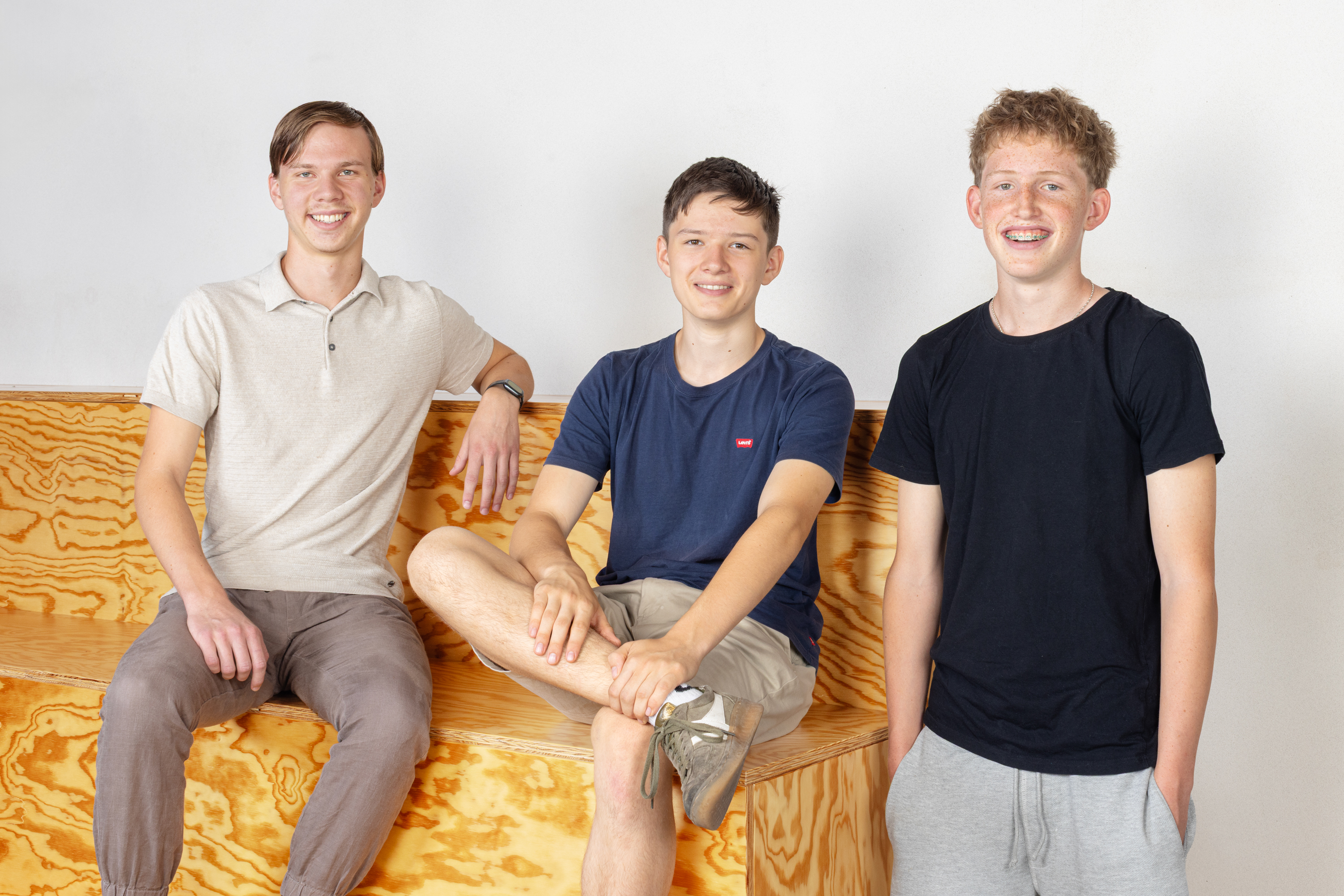 Eine Gruppe von drei Lernenden auf einer Holztreppe vor einer weissen Wand.