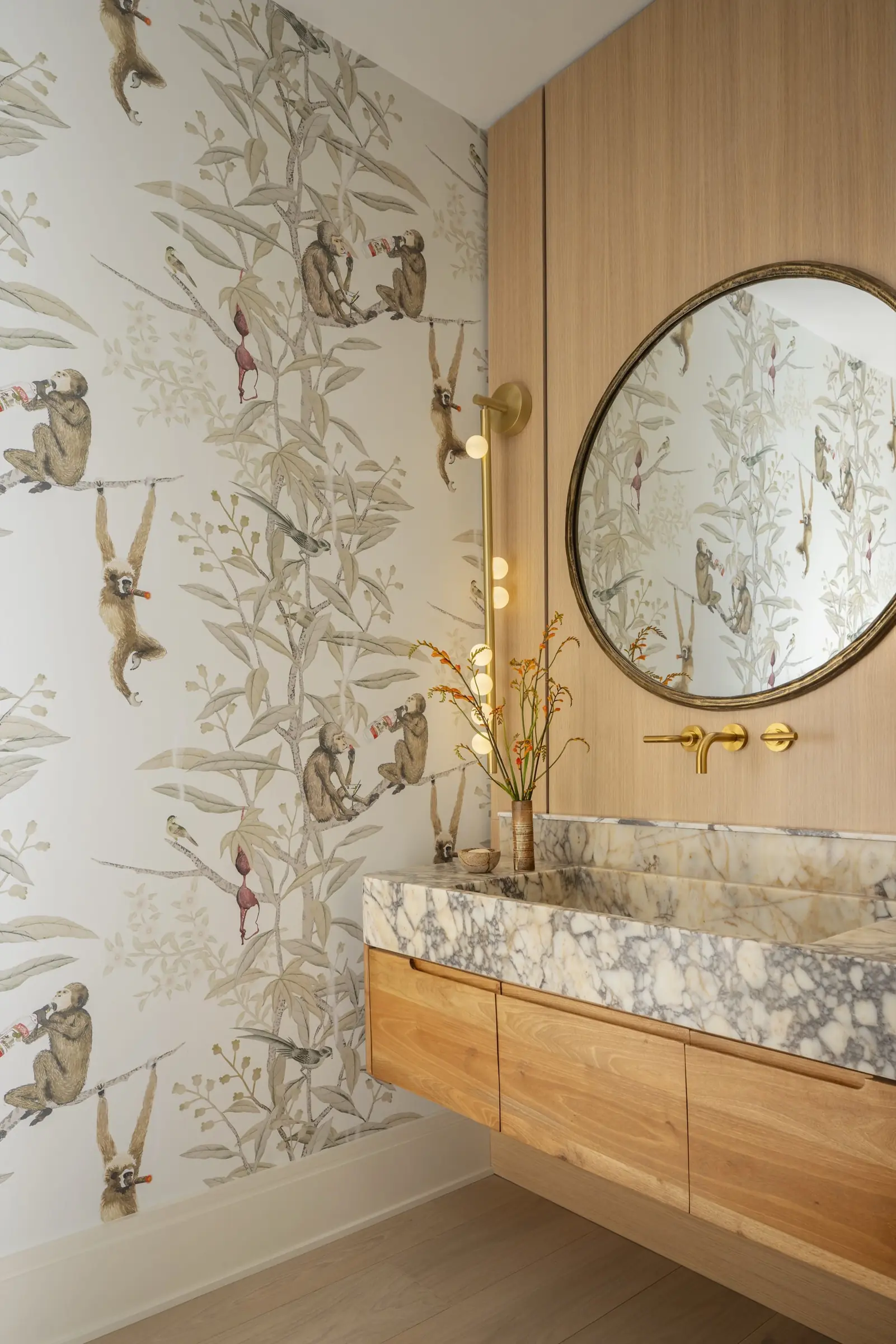 Powder room with illustrated animal wallpaper and round brass-framed mirror