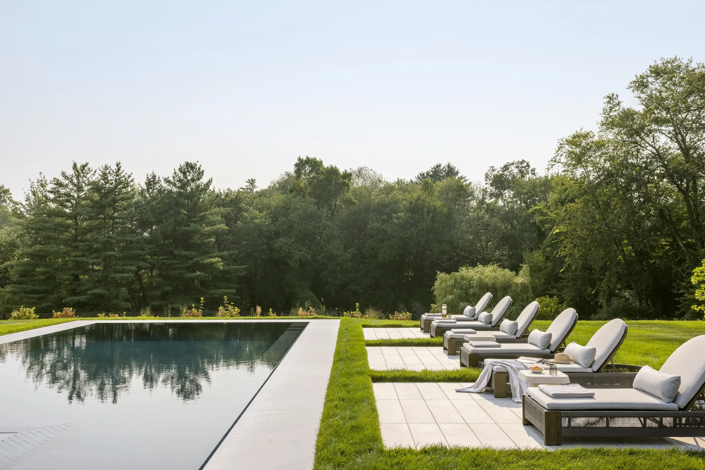 Outdoor pool and lounge area bordered by mature trees