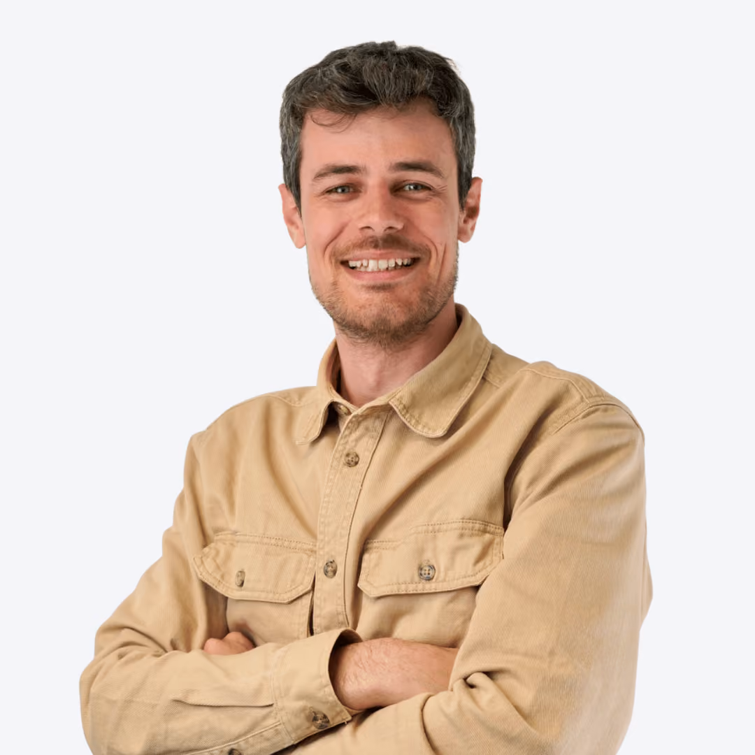 Man with short dark hair and beard wearing a blue blazer and white shirt with forest background.
