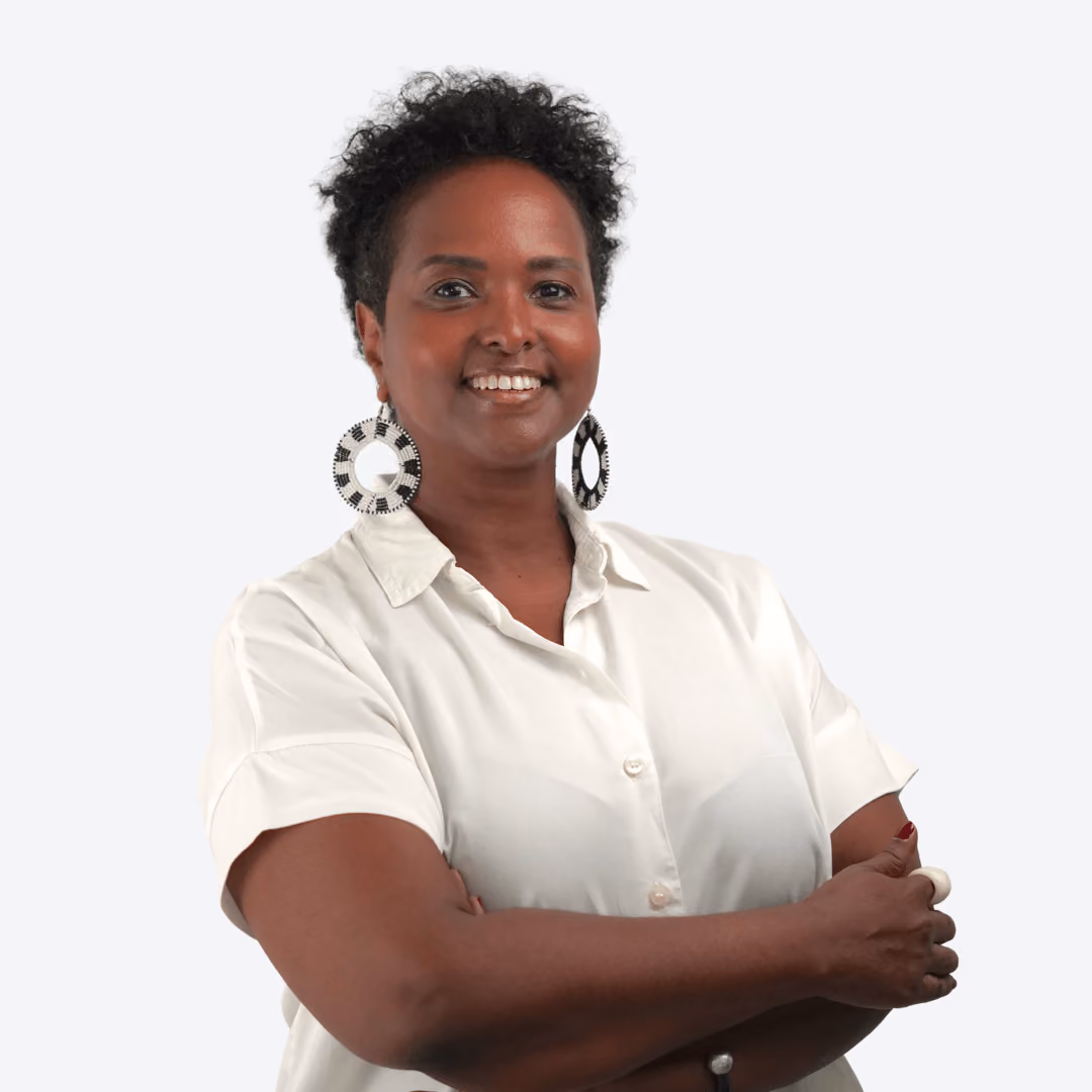 Smiling woman with curly hair and white earrings against a blurred green foliage background.