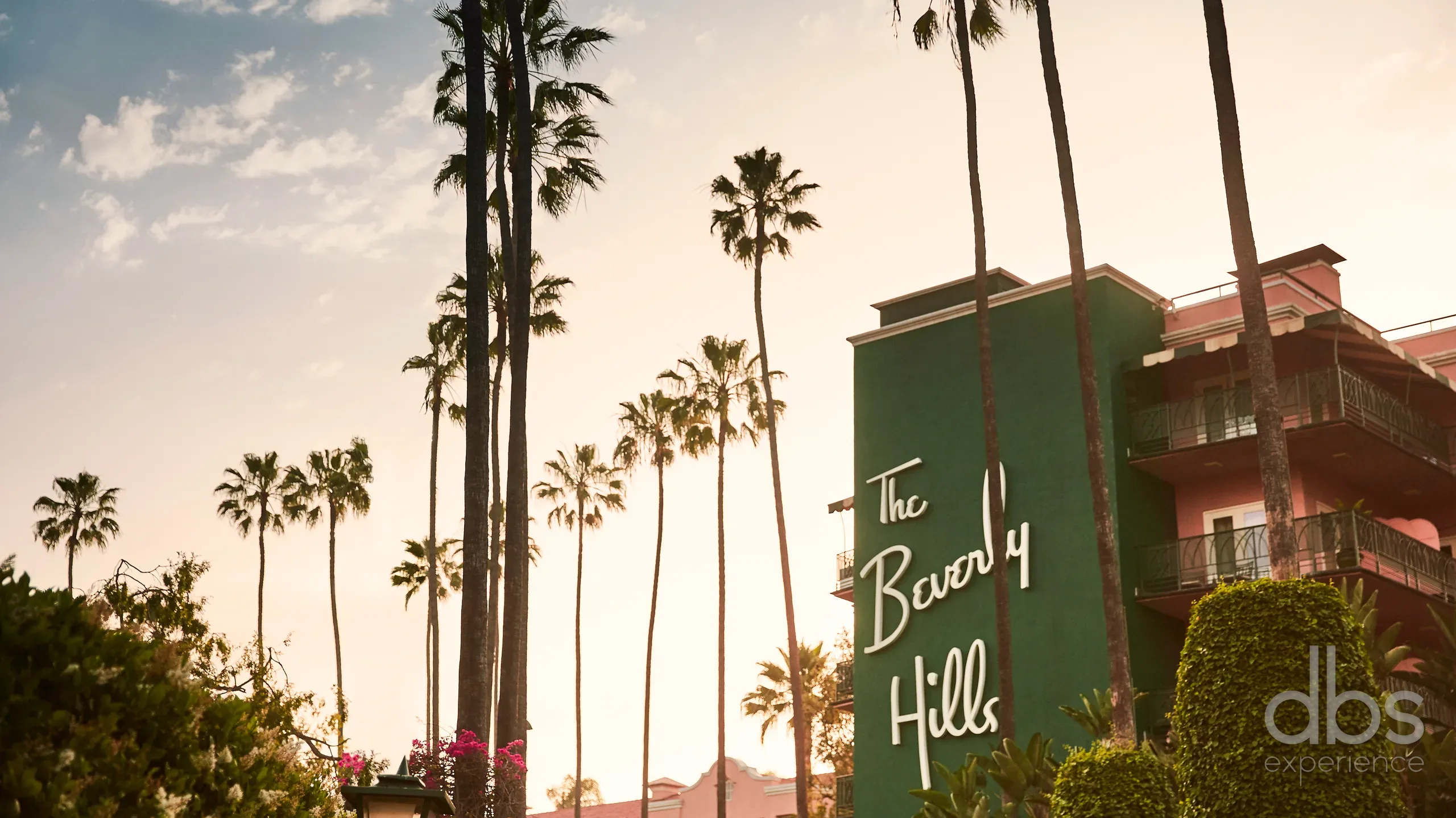 The Beverly Hills Hotel sign on a green tower framed by tall palm trees at sunset