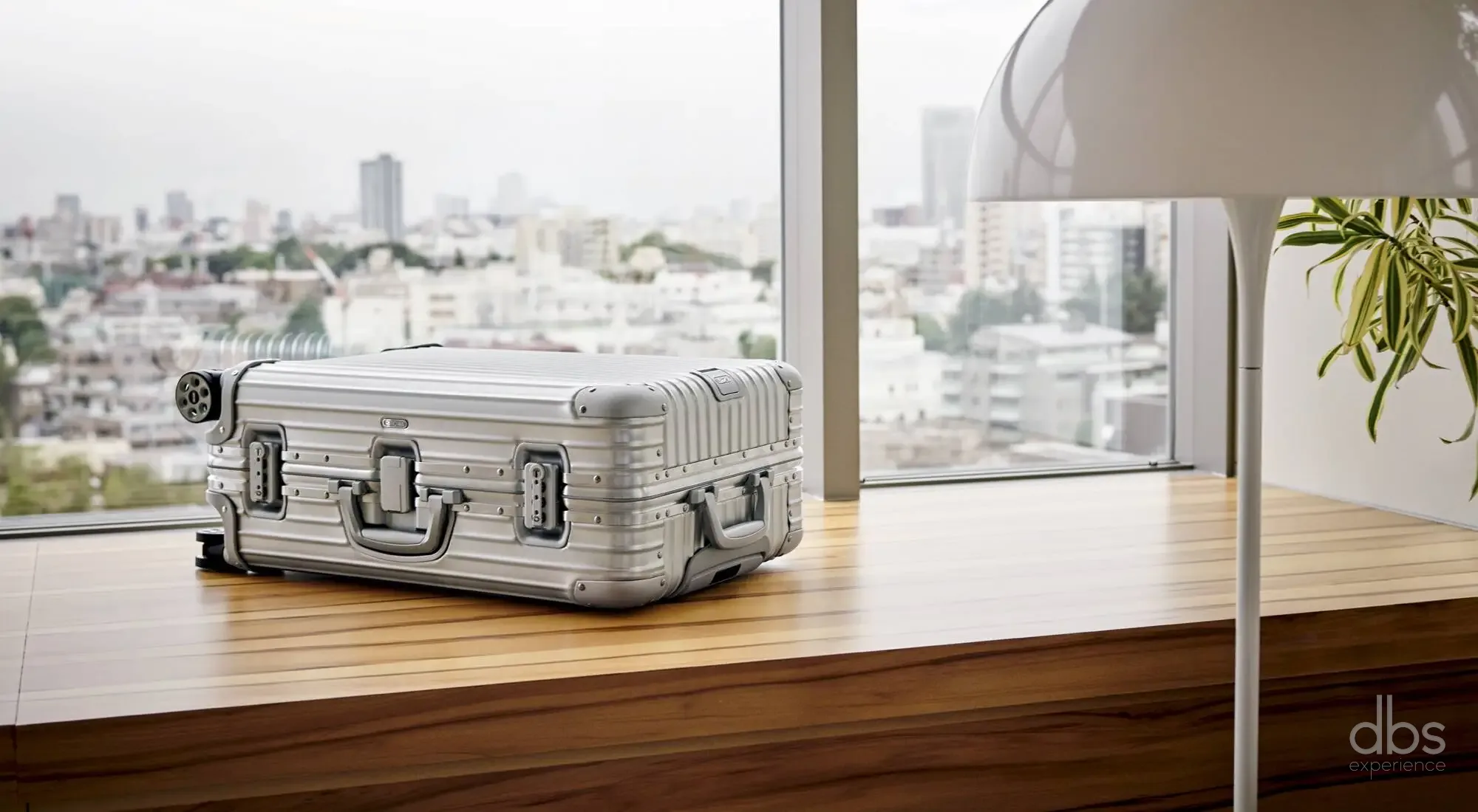 A designer aluminium suitcase by a window overlooking the city